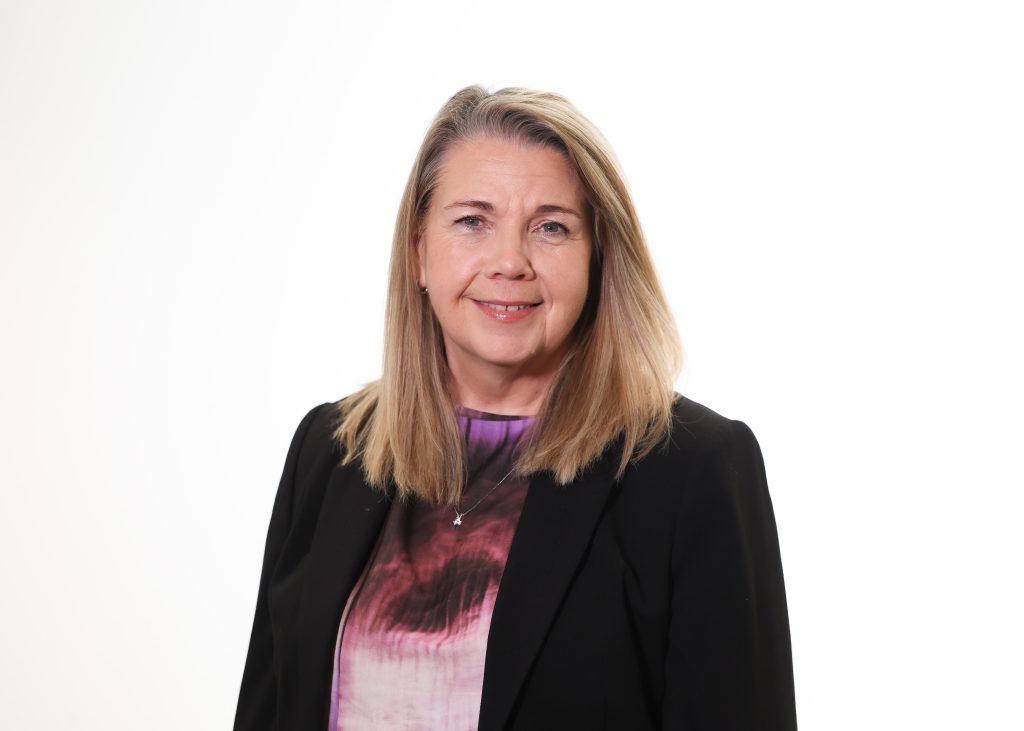 An image of Michelle Hawkins wearing a black blazer and purple top. She is smiling at the camera.