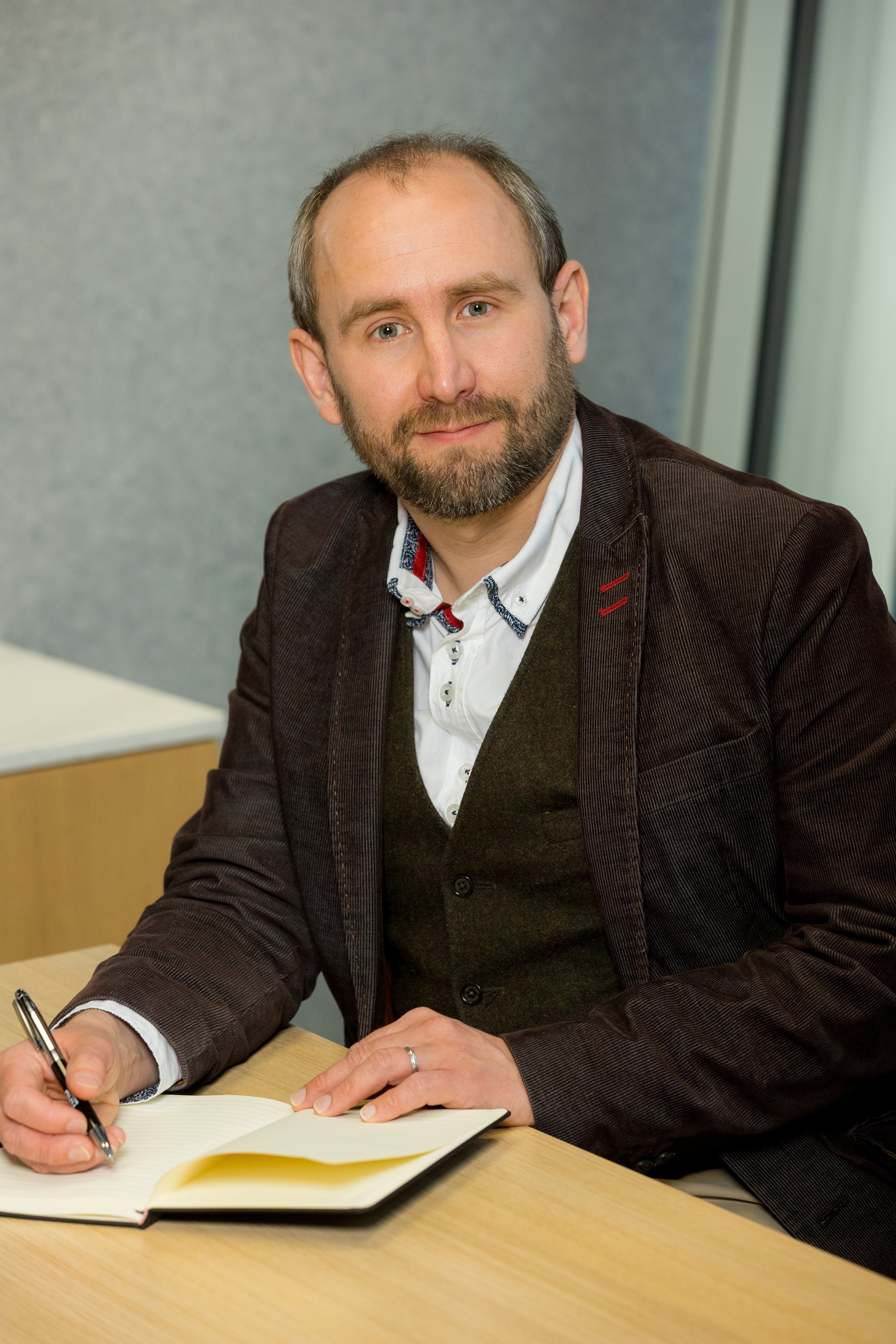 An image of Matthew Millyard sitting at a desk and writing in their notebook.