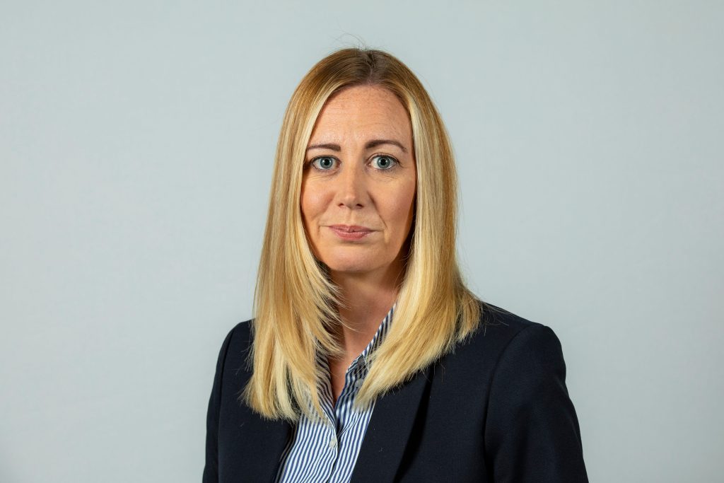 An image of Leanne Foster wearing a black suit jacket and blue shirt.