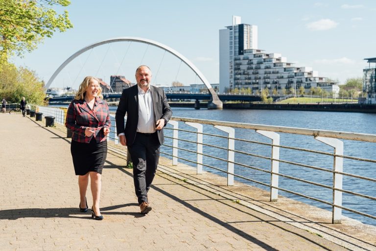 AAB employees Jude and David walking alongside the River Clyde in the sun.