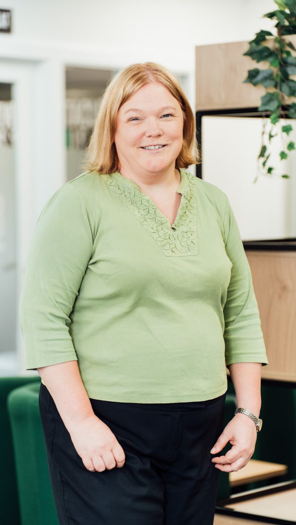 An image of Susan McKechnie standing in the office wearing a green top and black trousers.
