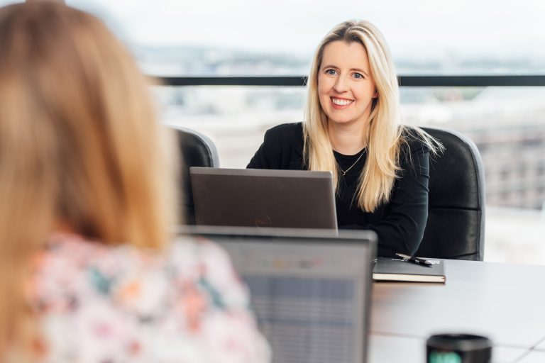 AAB team member on smiling at colleague across meeting room.