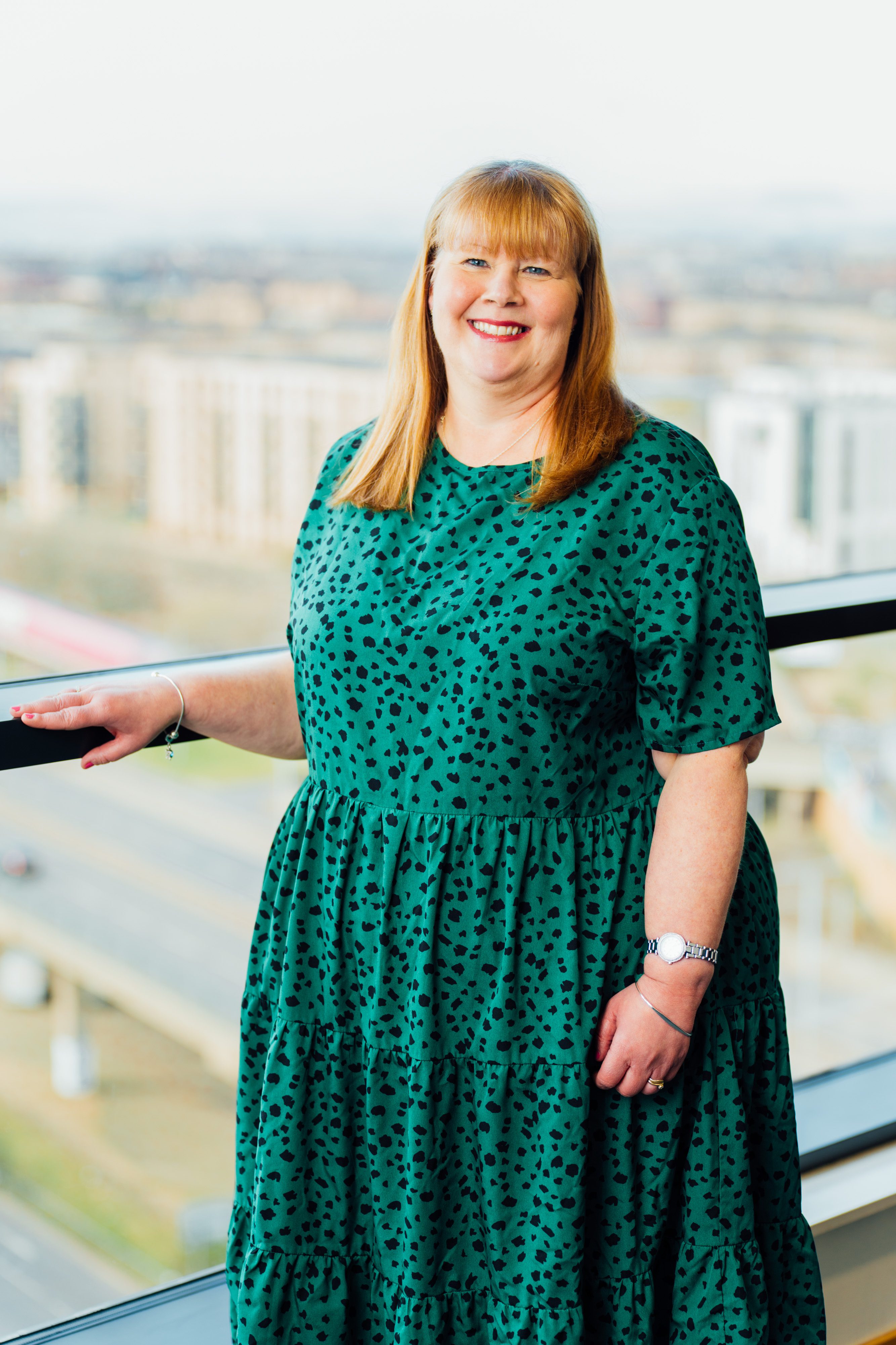An image of an AAB employee standing next to a window in a green dress.