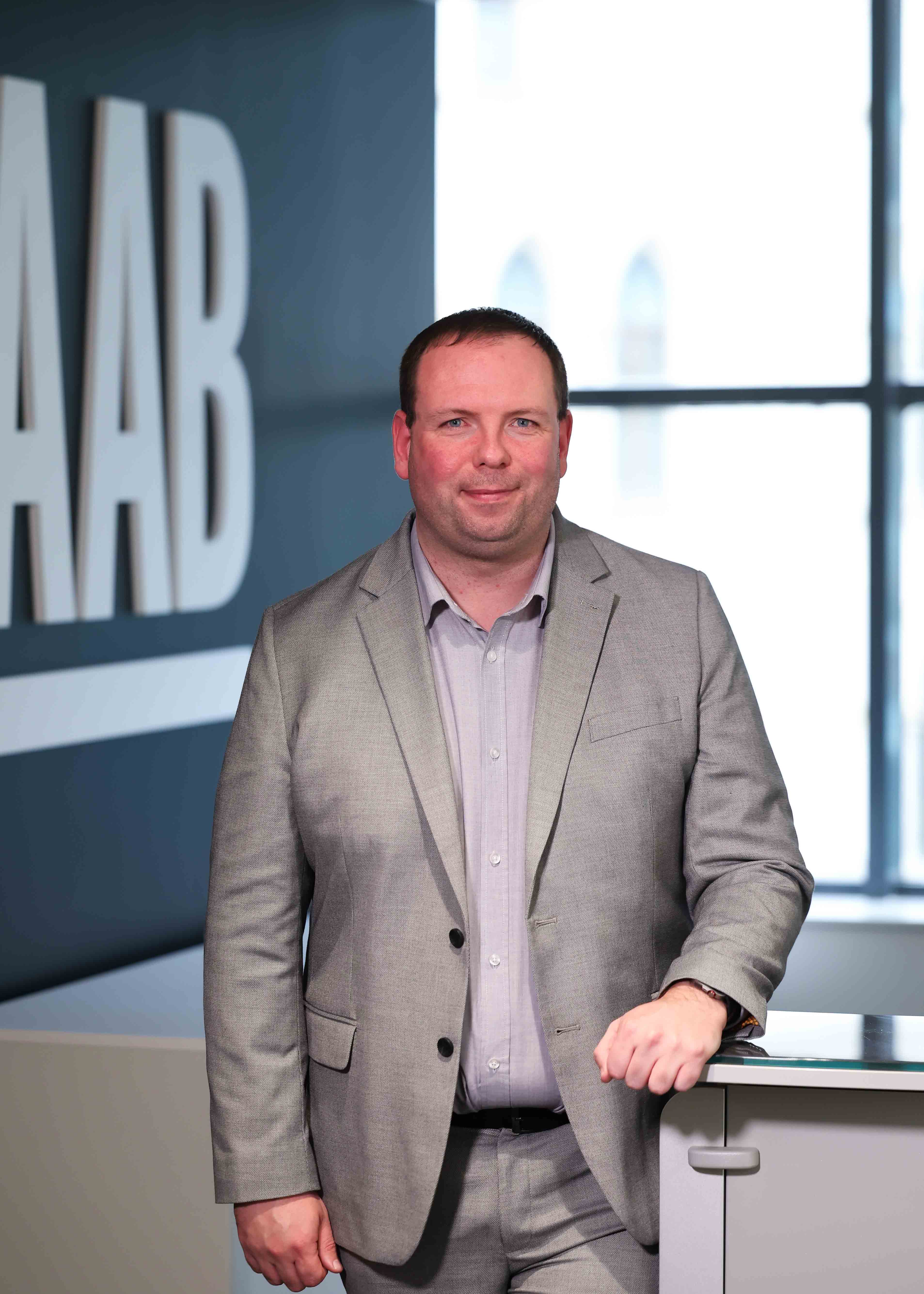 An image of Ryan McKernon wearing a grey suit and standing in the office.