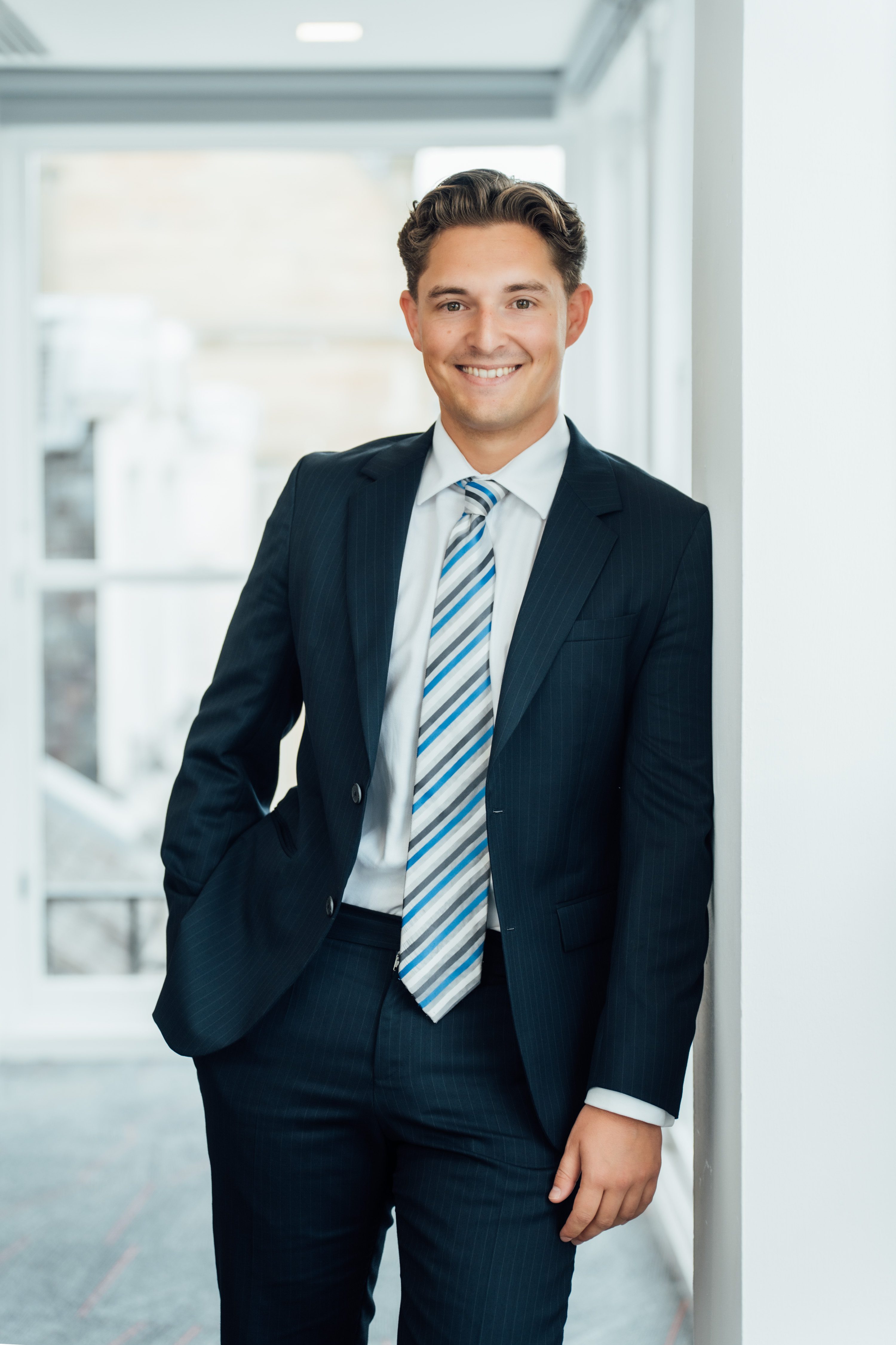 An image of Jack Martin wearing a suit with a tie and leaning against a wall.