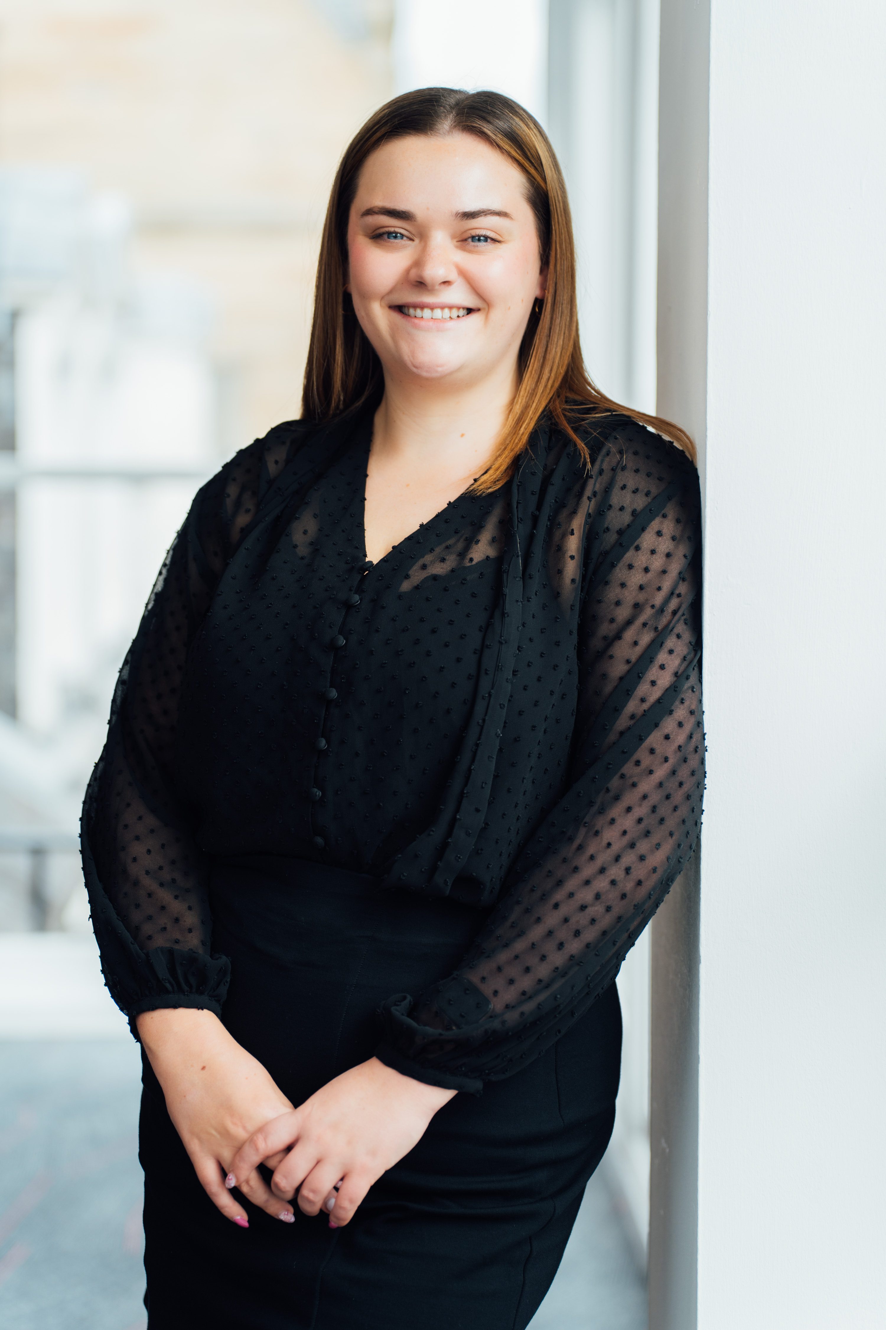 An image of Amy McLaughlin standing agaisnt a wall wearing a black outfit and smiling at the camera.