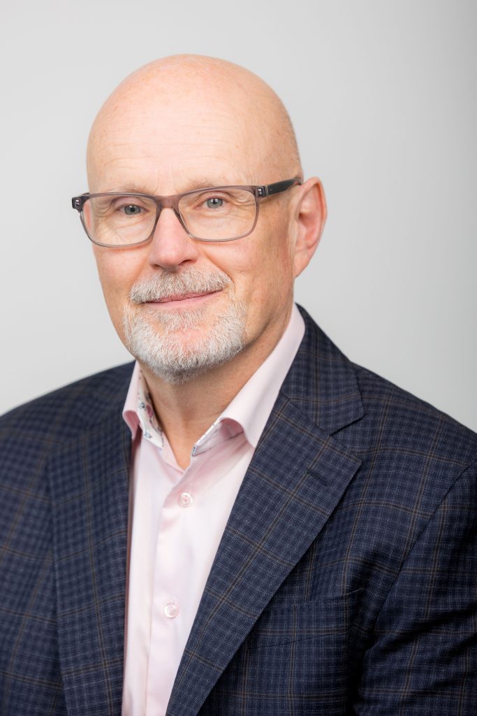 An image of Michael Aitken wearing a shirt and suit jacket whilst looking at the camera.