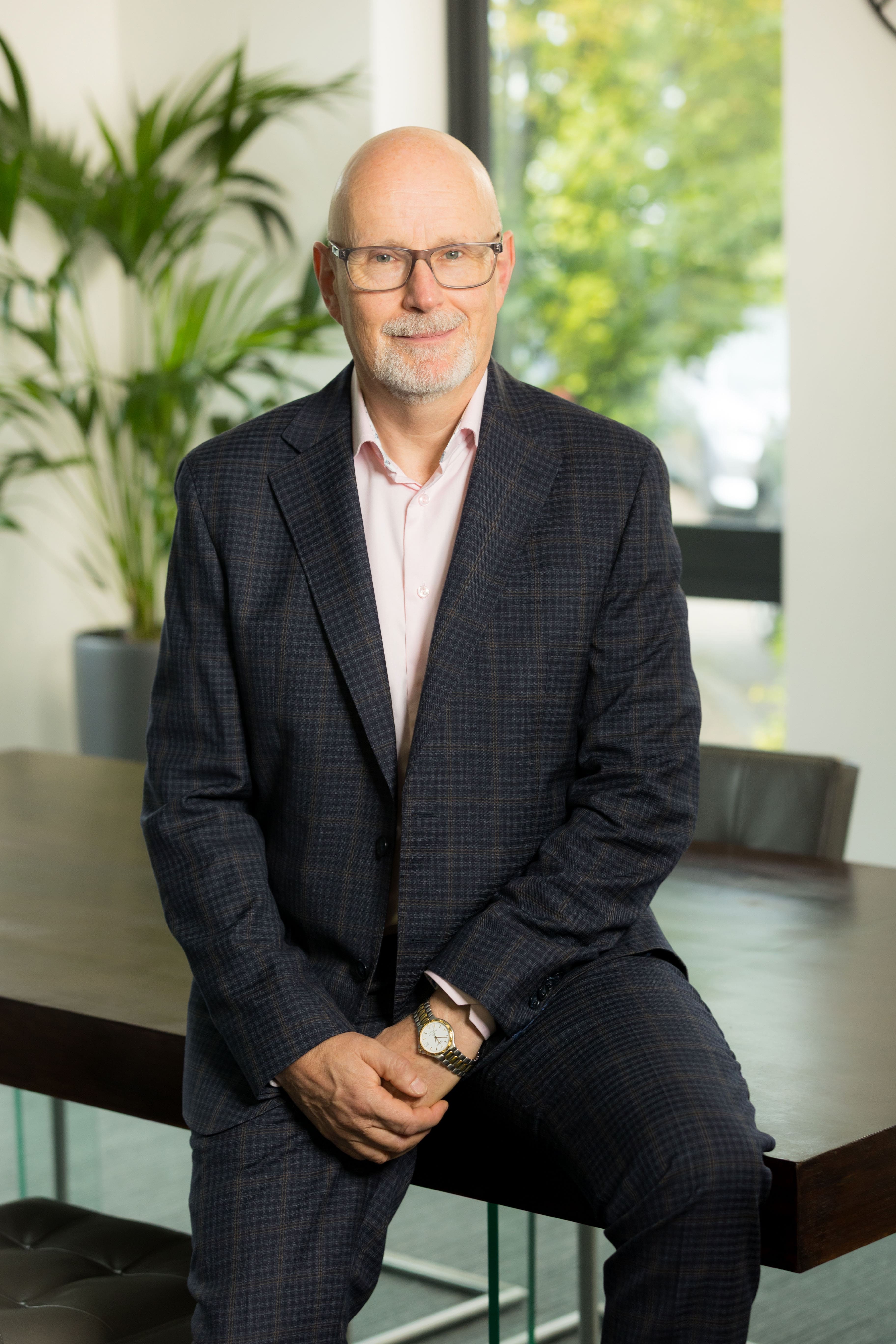 An image of Michael Aitken leaning on a desk with his hands crossed and smiling at the camera.