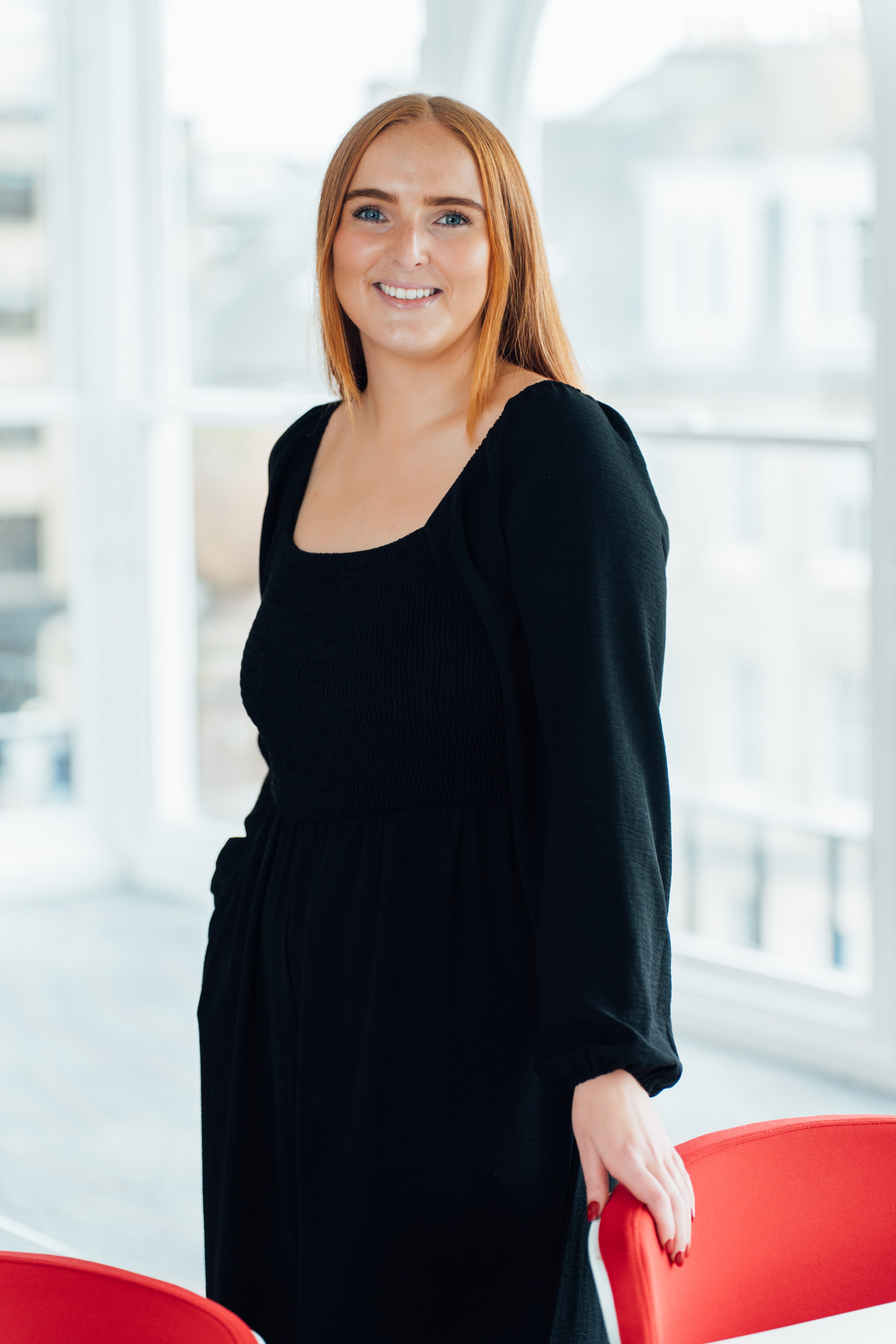 An image of Becky Weir standing in the Edinburgh office wearing a black dress and smiling at the camera.