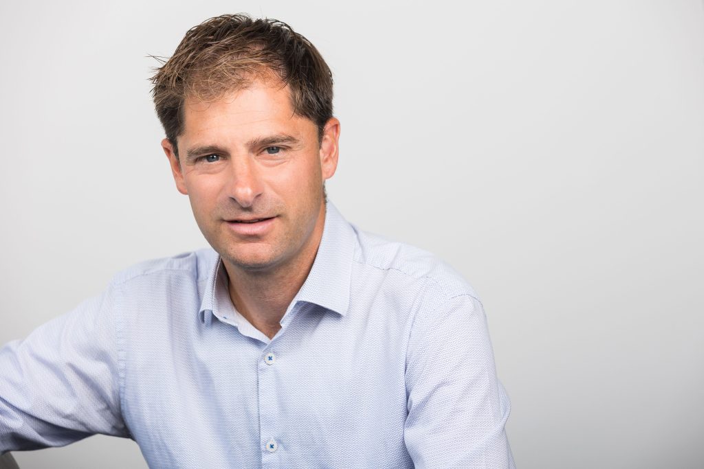 An image of Colin Judd wearing a blue shirt and smiling at the camera.
