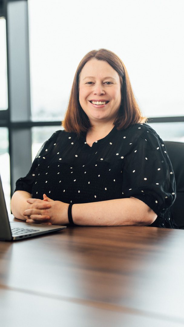 An image of Debra Duffy sitting at a desk with her laptop and smiling at the camera.