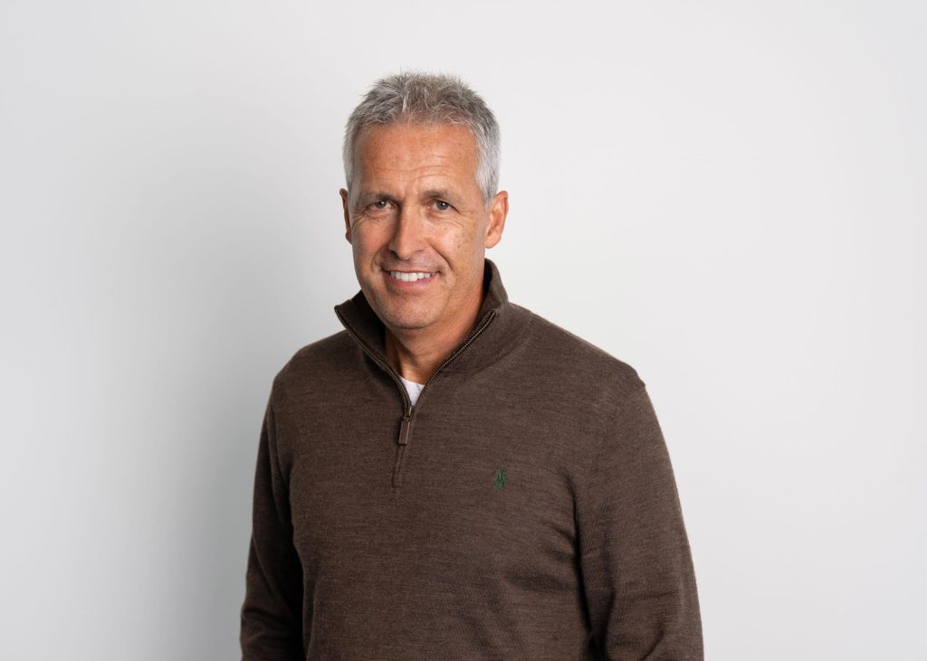 An image of Glenn Brophy smiling at the camera wearing a brown jumper.