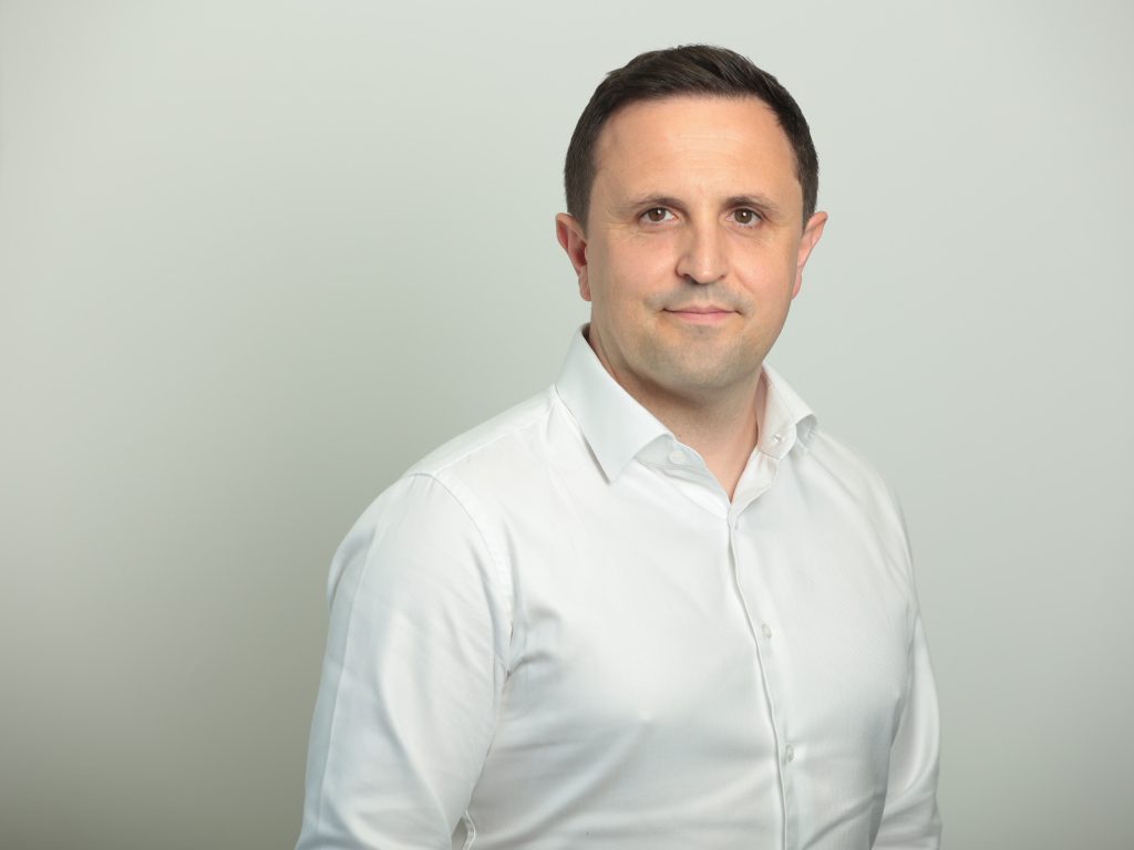 An Image of Andy Gardner wearing a white shirt and smiling at the camera.
