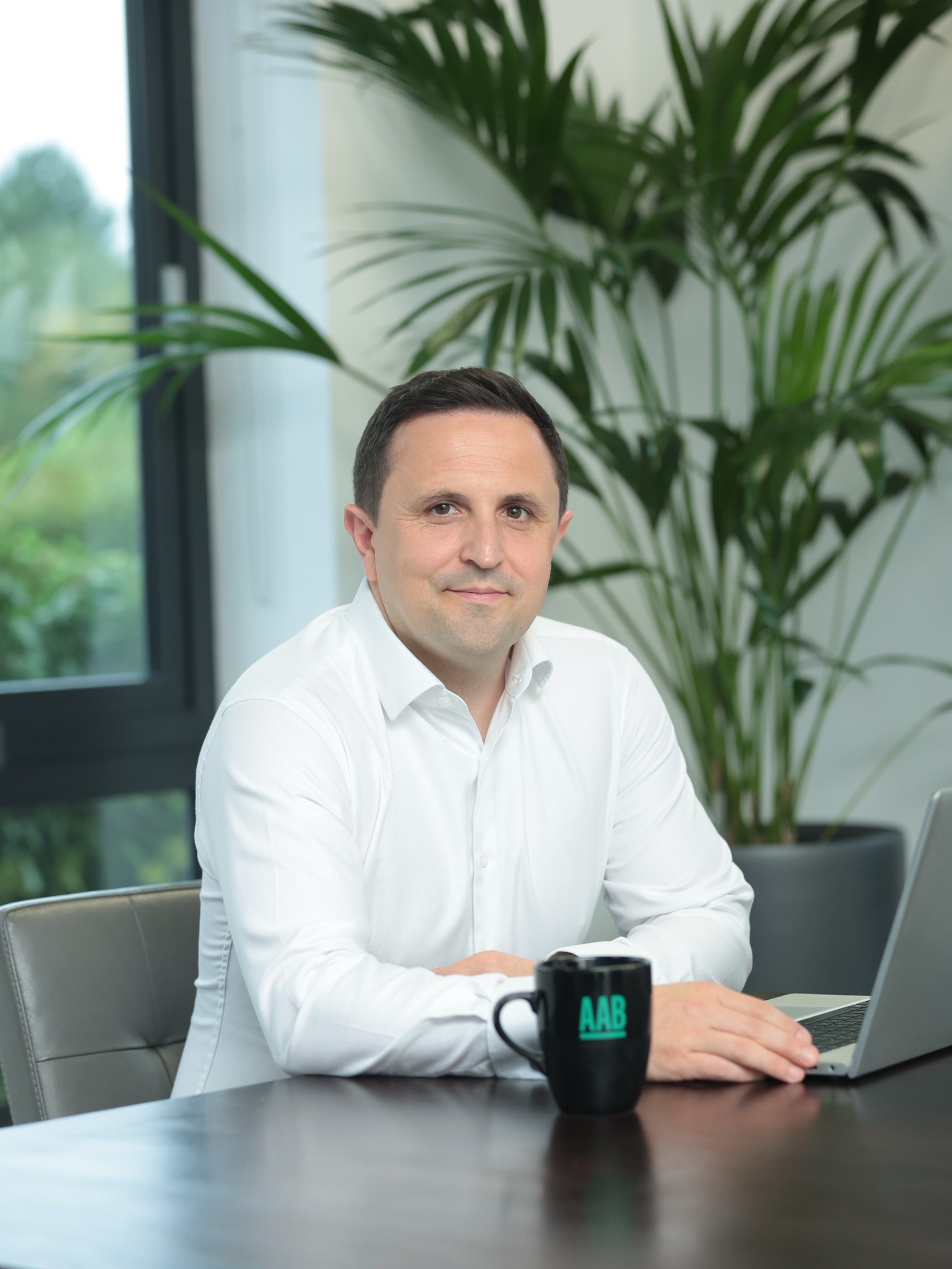 An image of Andy Gardner wearing a shite shirt and sitting at a desk with a laptop and AAB branded mug.