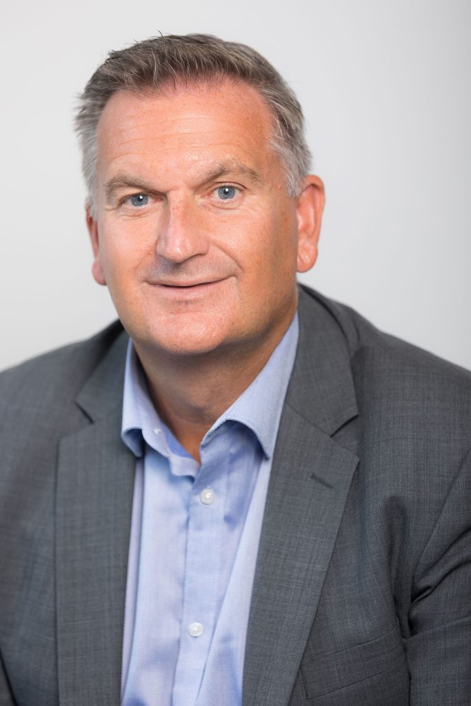 An image of James West wearing a blue shirt and grey suit jacket.