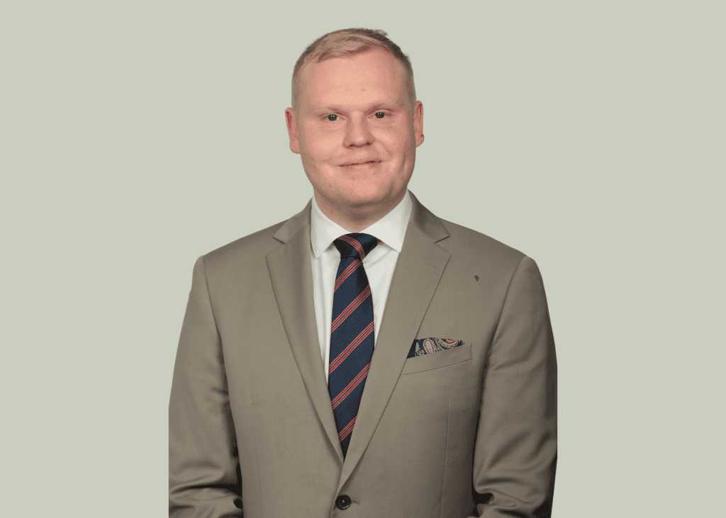 An image of Matthew Knight wearing a beige suit and tie.