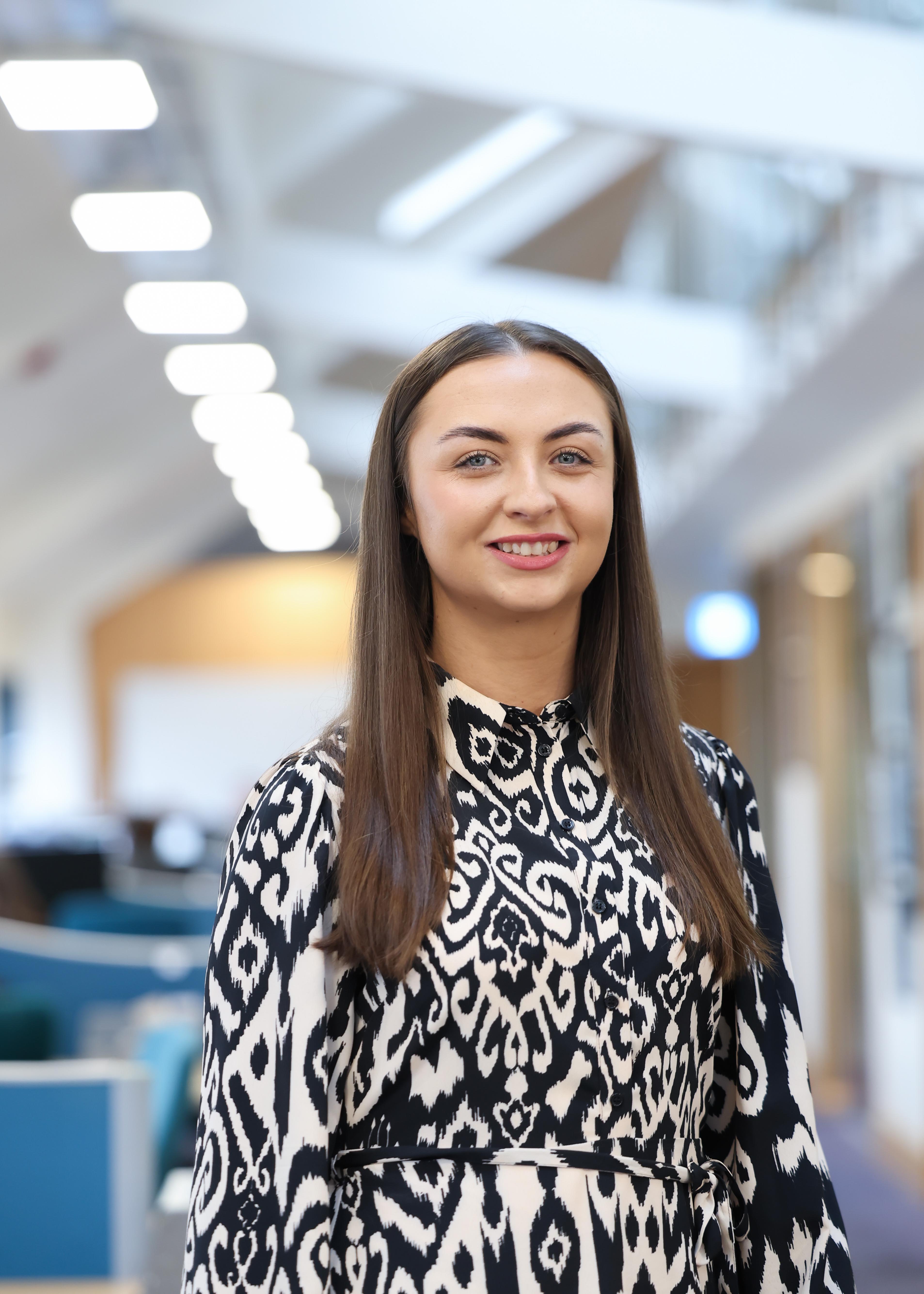 An image of Nisha Teeling wearing a black and white top, and standing in the office.