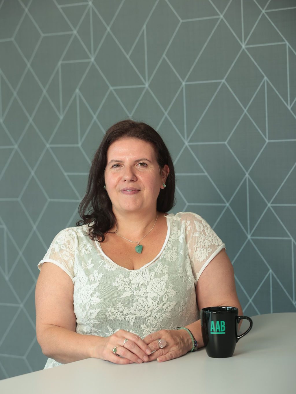 An image of Abi Cornish wearing a white top and sitting at her desk with an AAB branded mug.
