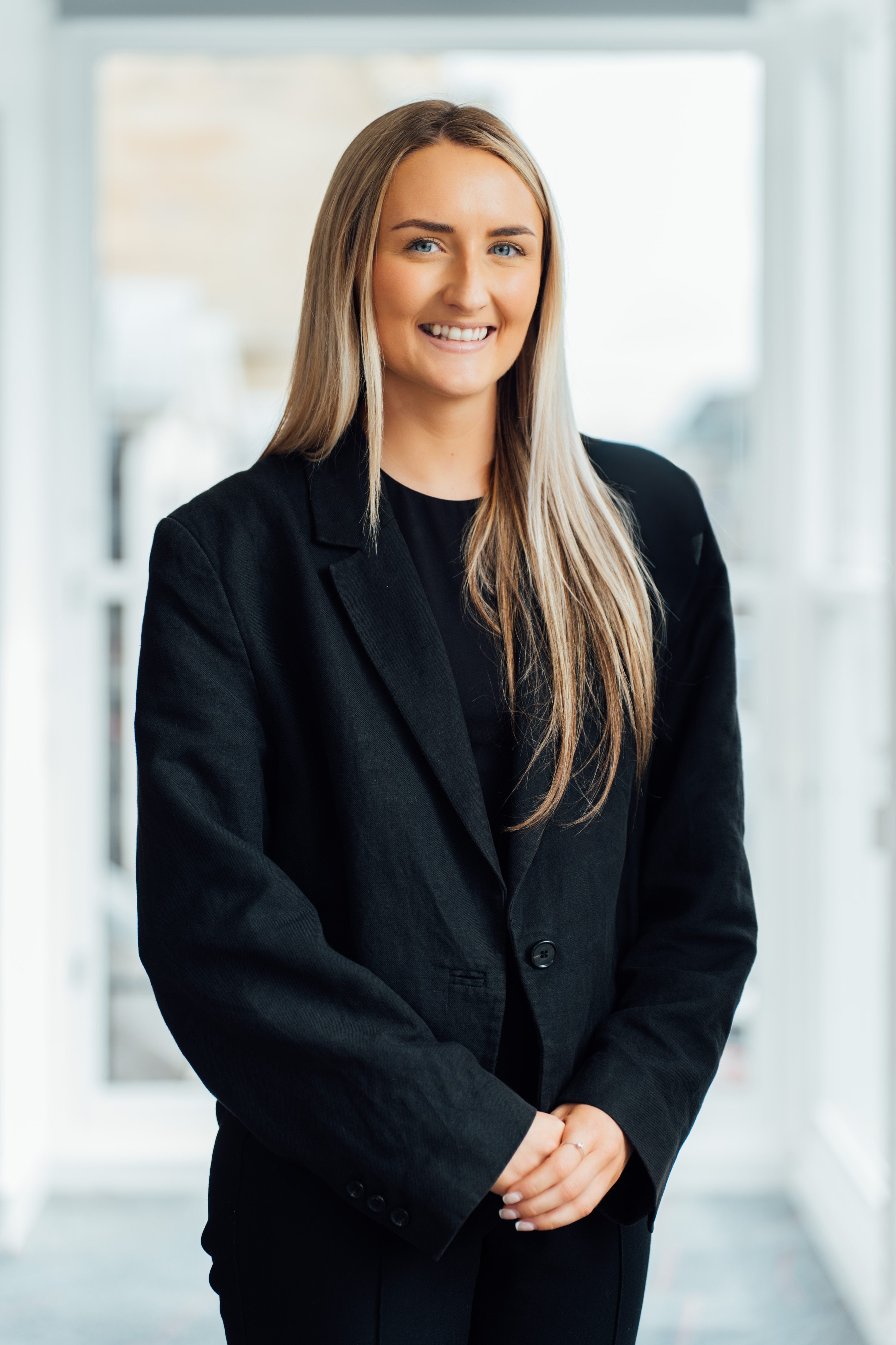 An image of Emily Ross standing against a wall and wearing a black blazer.