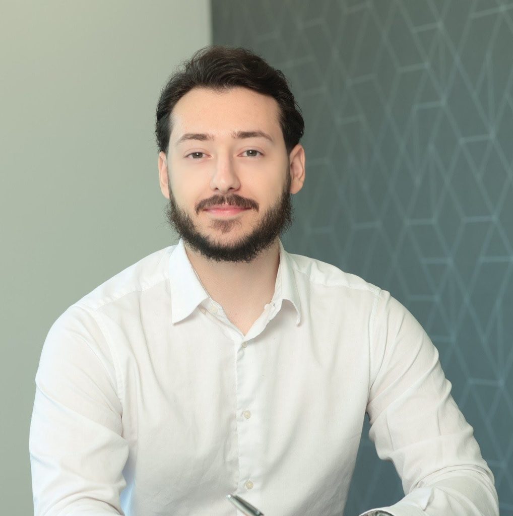 An image of Belmin Hadzic wearing a shite shirt and sitting at the desk. He is writing in his AAB Wealth notebook.