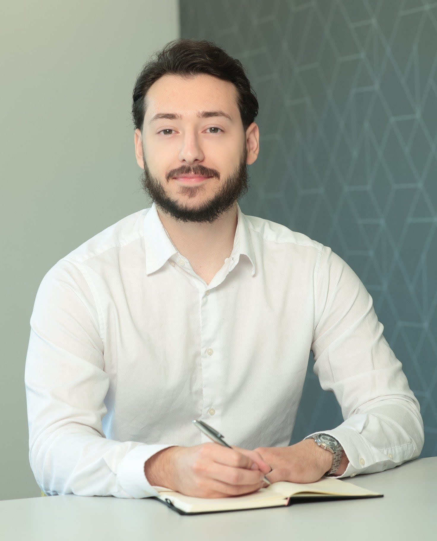 An image of Belmin Hadzic wearing a shite shirt and sitting at the desk. He is writing in his AAB Wealth notebook.