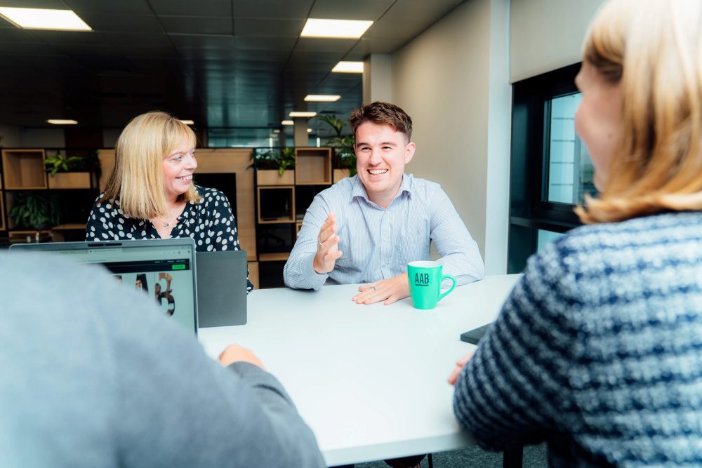 AAB team having a meeting in the Glasgow office breakout area, smiling and chatting to one another