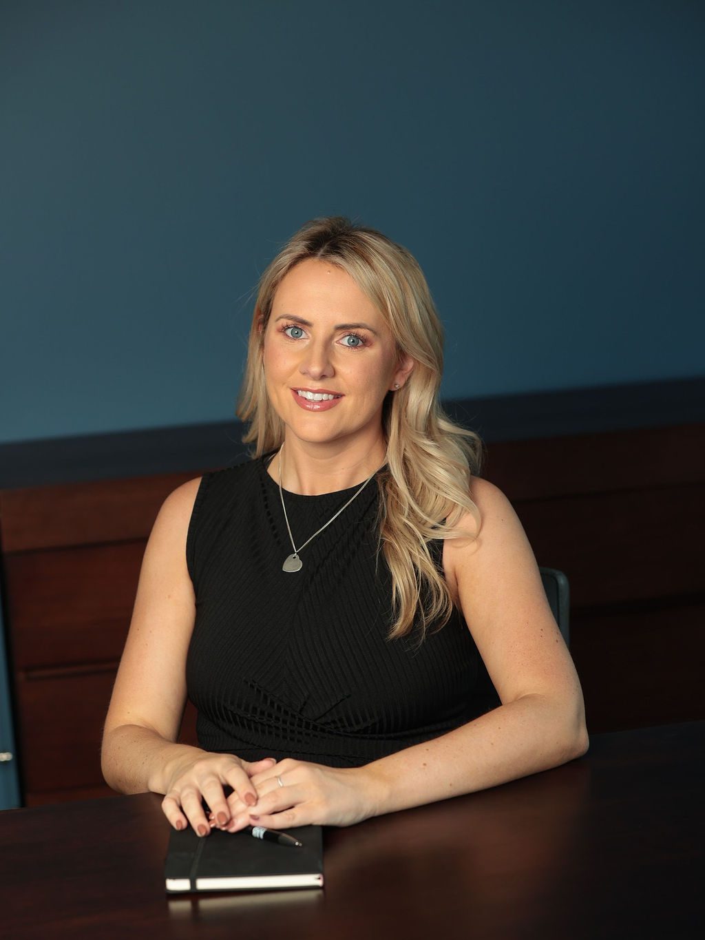 An image of Lianne Finnegan wearing a black dress and sitting at the desk with her AAB Wealth notebook.