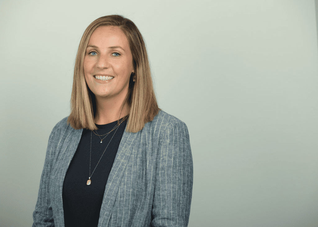 A headshot image of Victoria Minett wearing a grey blazer and black top.