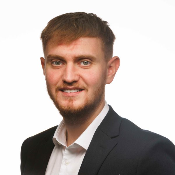 An image of Thomas Booth wearing a white shirt and black suit jacket.