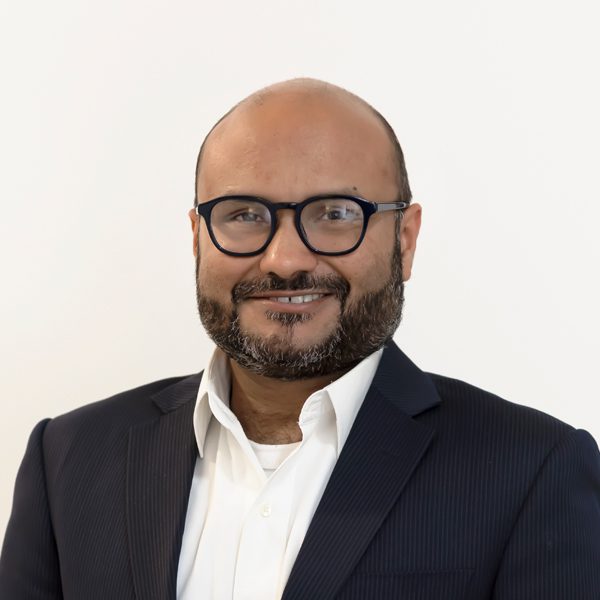 Muhammad Sharif in white shirt and black blazer smiling.