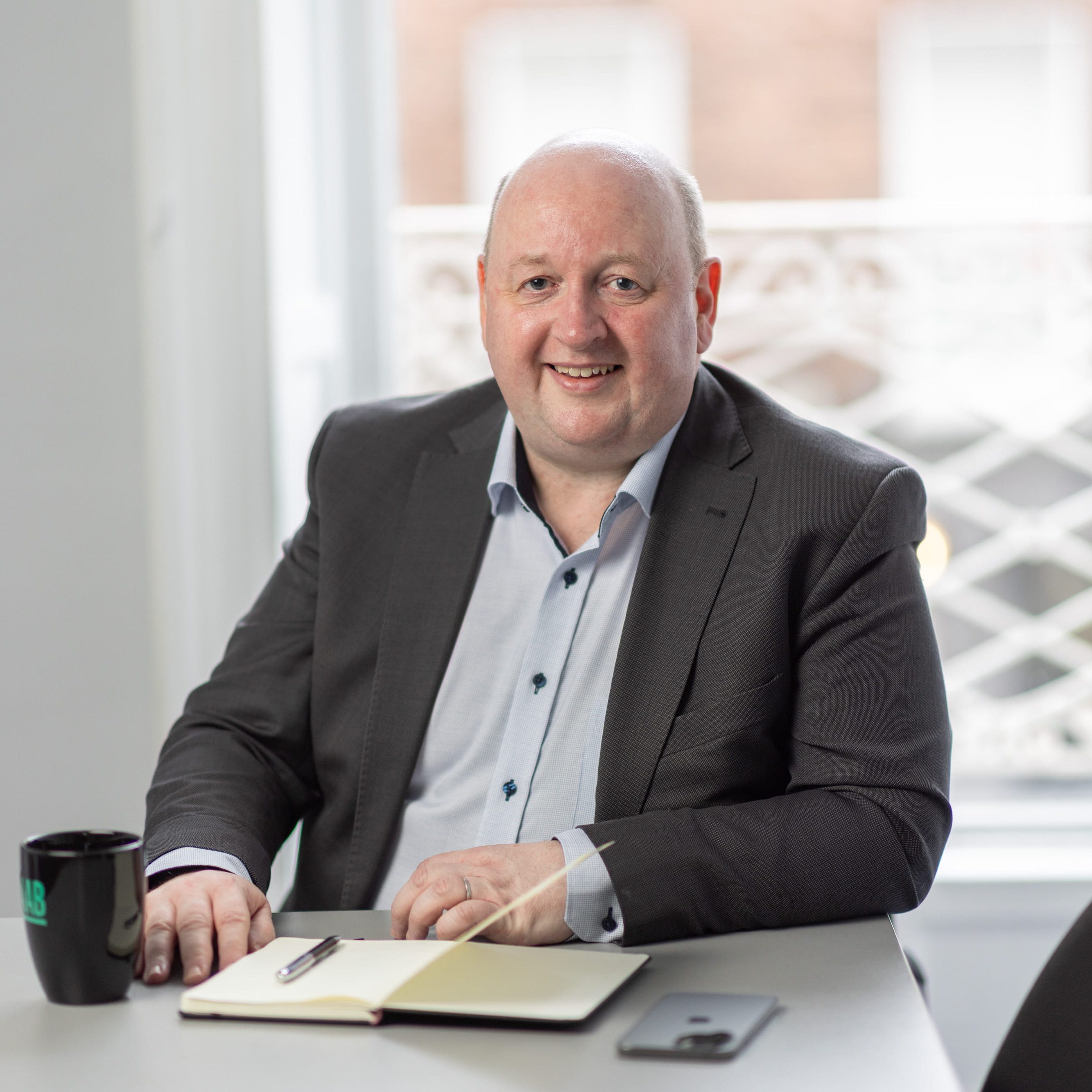 An image of Aidan McCarthy wearing a grey blazer and blue shirt. He is smiling at the camera.