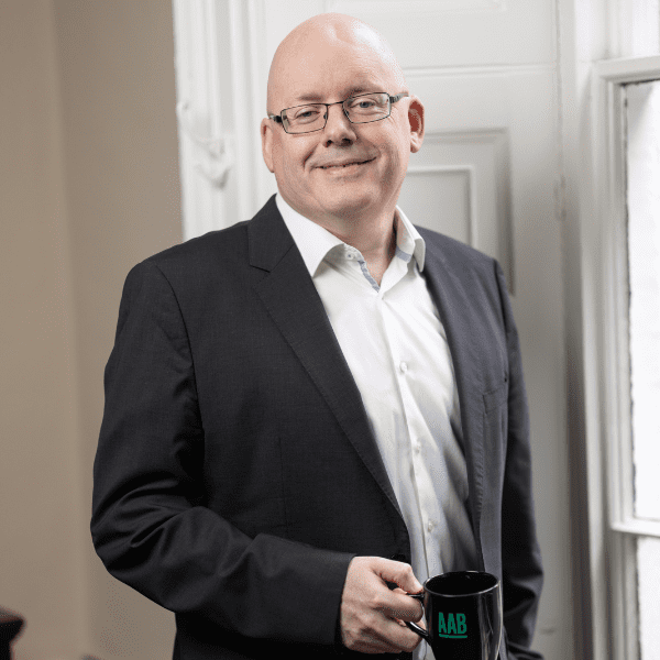 An image of Garret Wynne wearing a black suit jacket and white shirt. He is smiling at the camera.