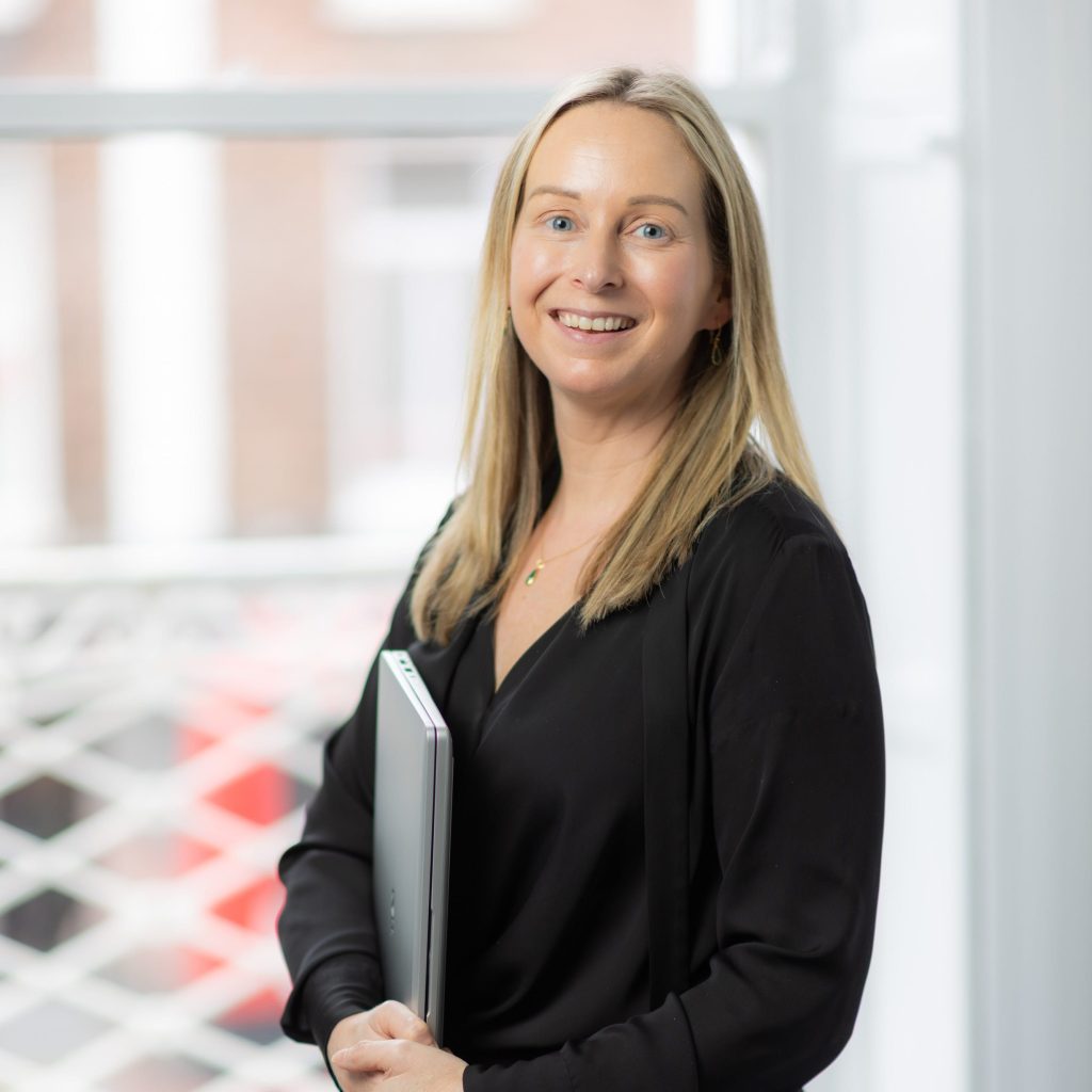 An image of Kate Mullahy wearing a black outfit and holding her laptop.