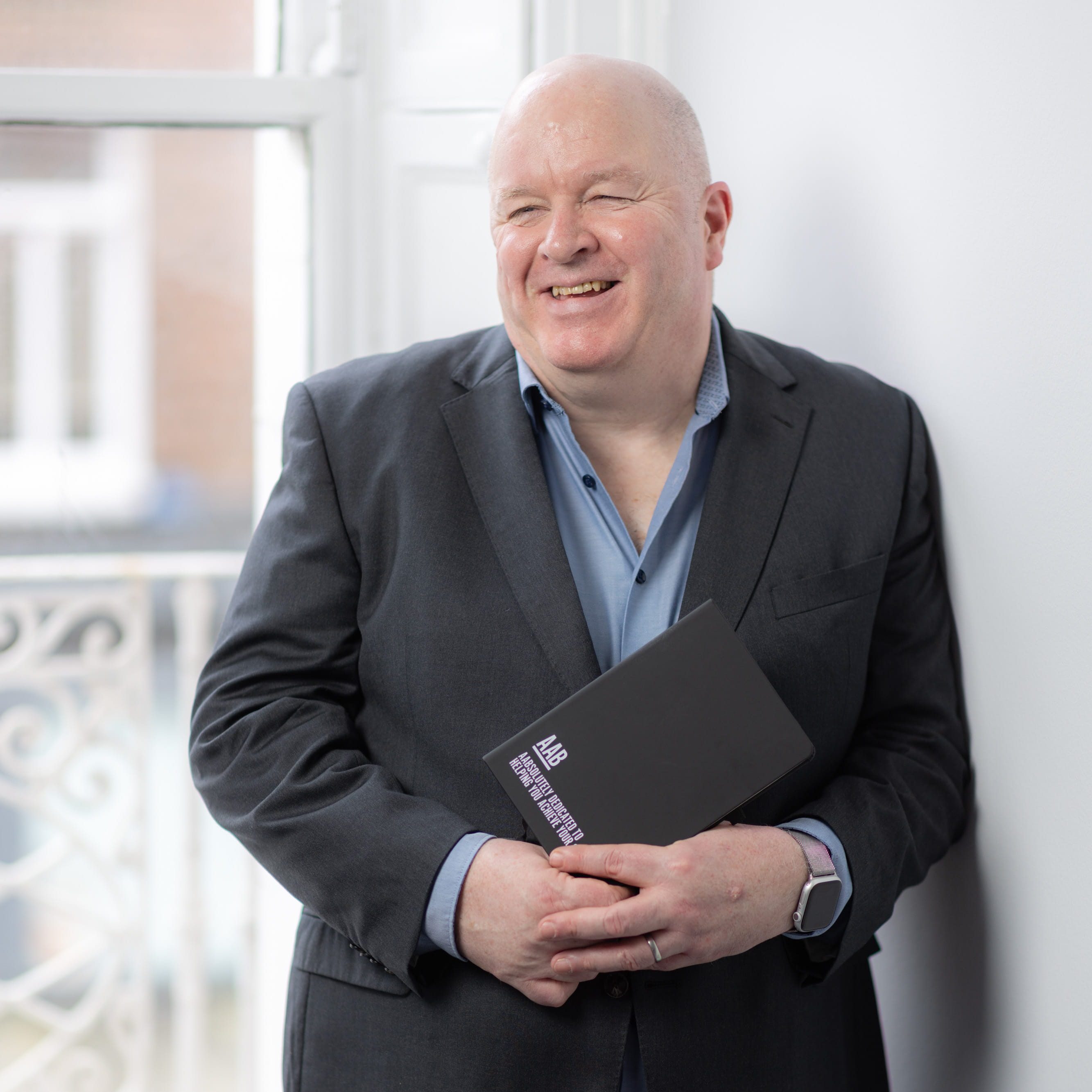 An image of Justin Brady standing in the Dublin office holding his AAB notebook and smiling at a colleague.