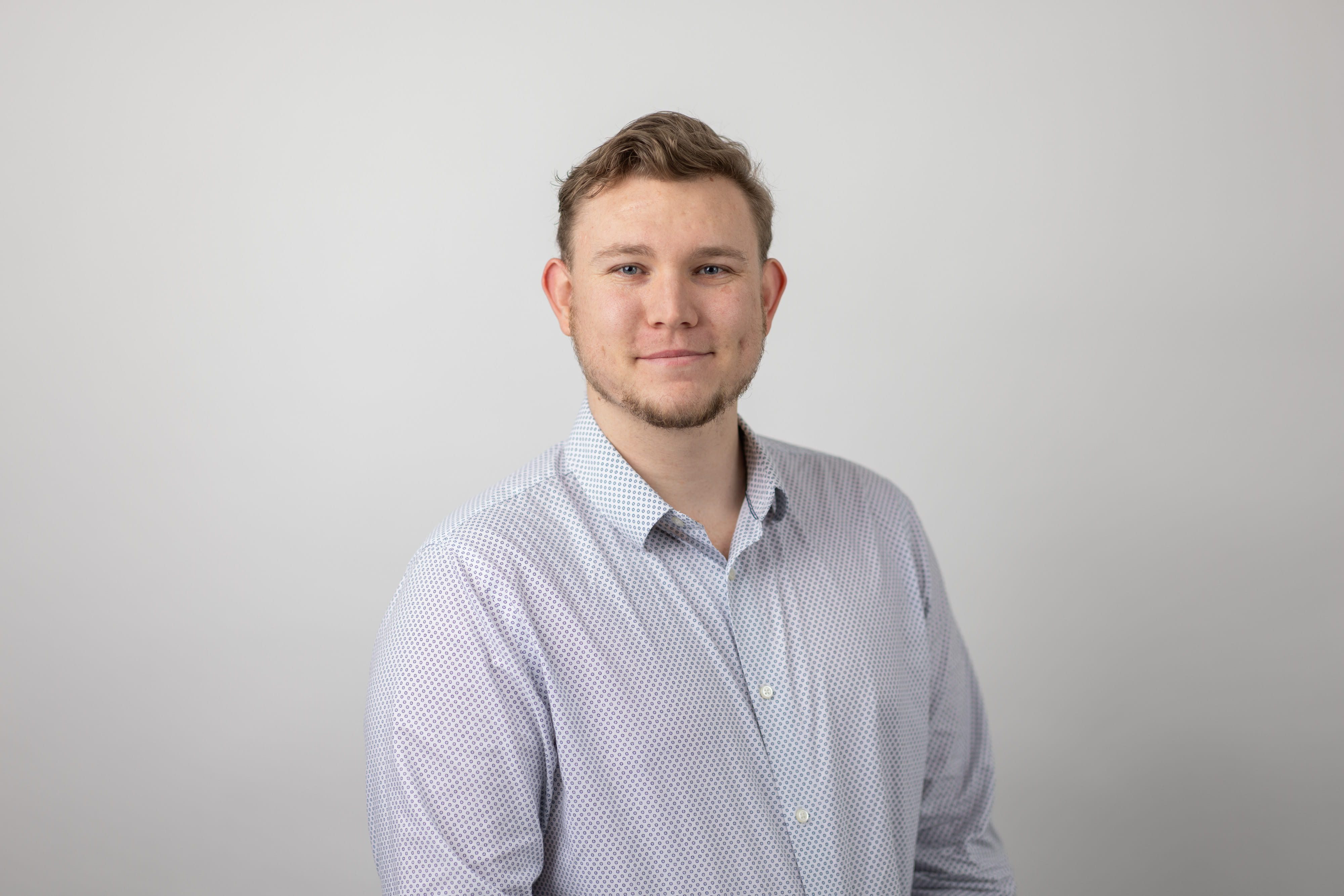 An image of Shane Brown smiling at the camera and wearing a blue shirt.