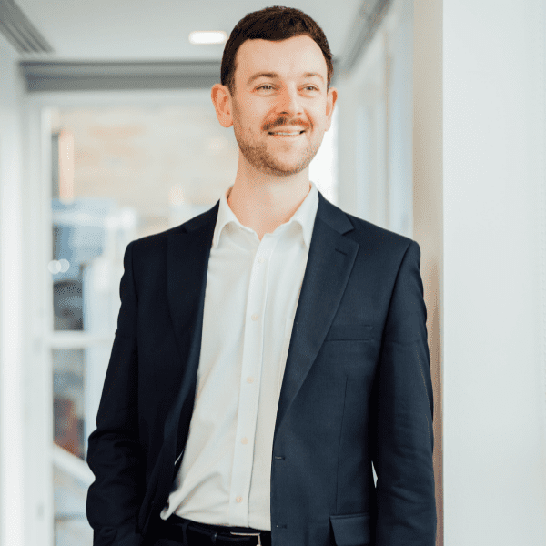 An image of Steven McCormick leaning against a window and wearing a dark coloured blazer and white shirt.