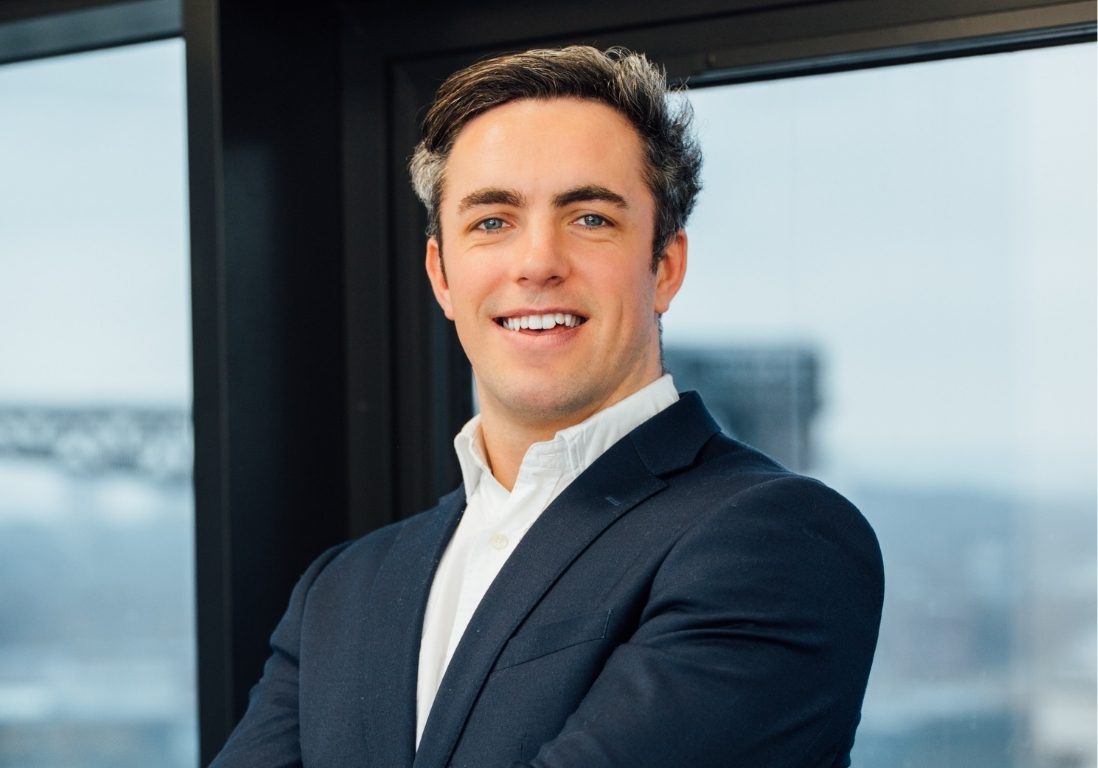 Daniel Lightbody smiling in the office with his arms folded and a view of Glasgow in the background