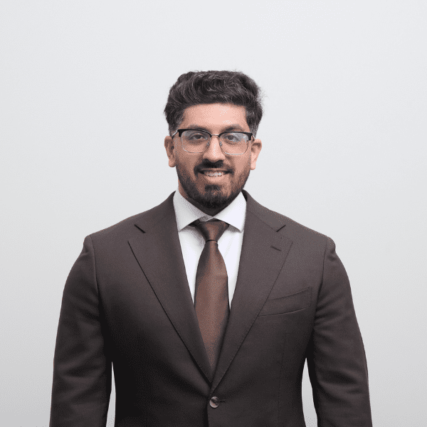 An image of Rafiq Gazi wearing a brown suit and tie. He is smiling at the camera.