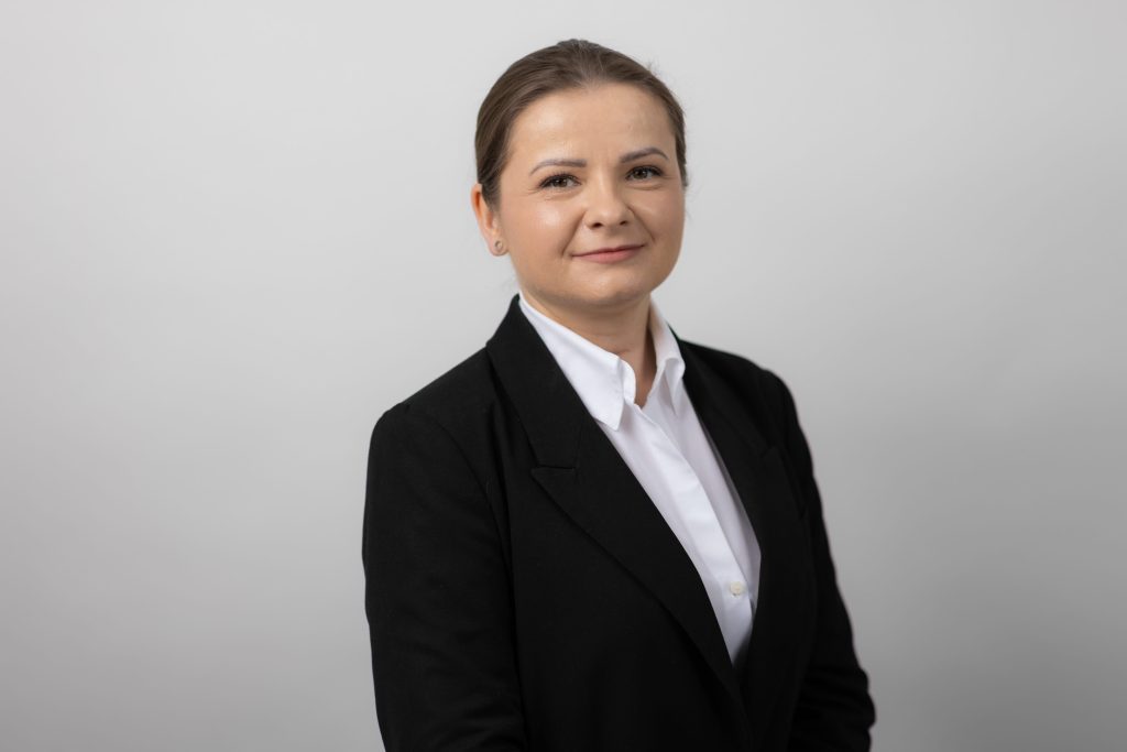 An image of Zoe Podraza wearing a black suit jacket and white shirt.