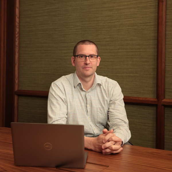 An image of George Barker sitting at a desk and smiling at the camera.