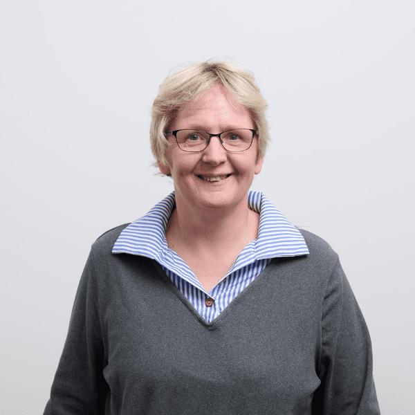 An image of Trudy Parling wearing a grey top and blue shirt. She is smiling at the camera.