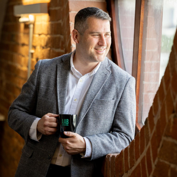 An image of David Dulieu looking out the window and smiling at the camera. He is holding an AAB mug.