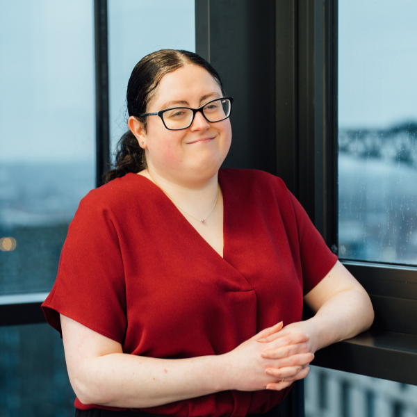 An image of Natalie Kelly standing in the office and wearing a red top.