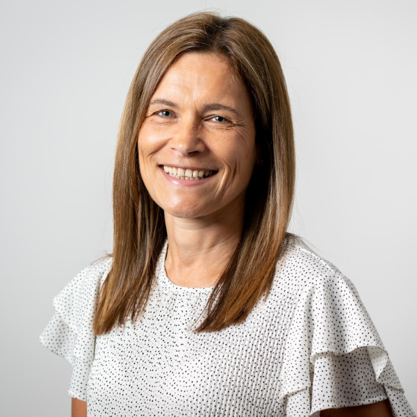 Emma Jones, Associate Director at AAB, has middle length brown hair and wears a white spotted top with flary, two layer sleeves.