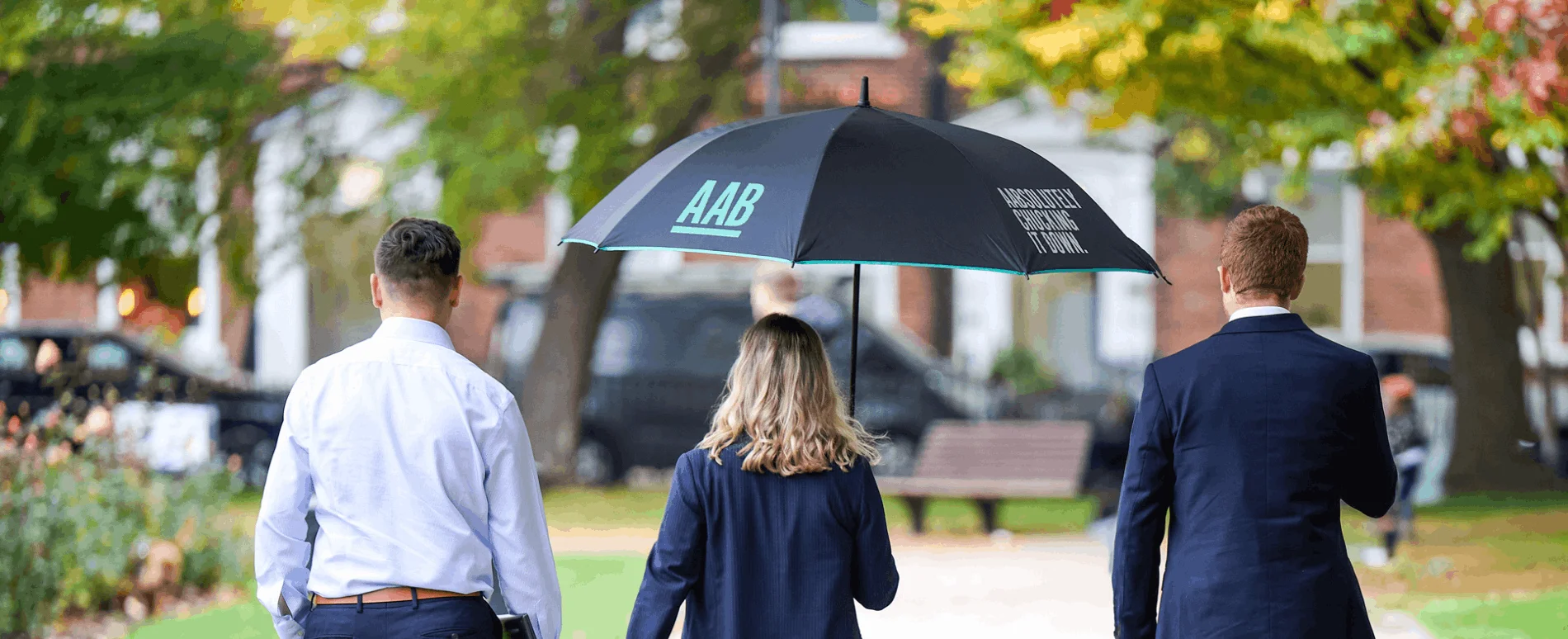 An image of three AAB employees walking and holding an umbrella.