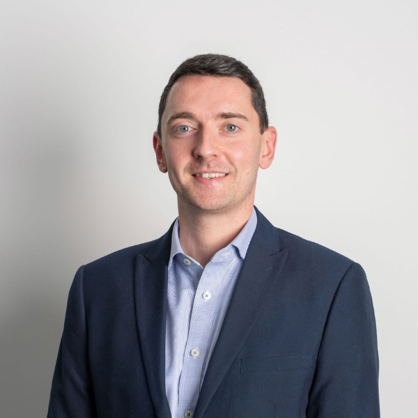 Head and shoulders shot of Stuart Riley smiling against a grey backdrop